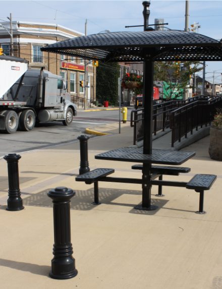 An attractive, solid black patio set with umbrella on a municipal sidewalk in Caledonia. A truck passes in the background.